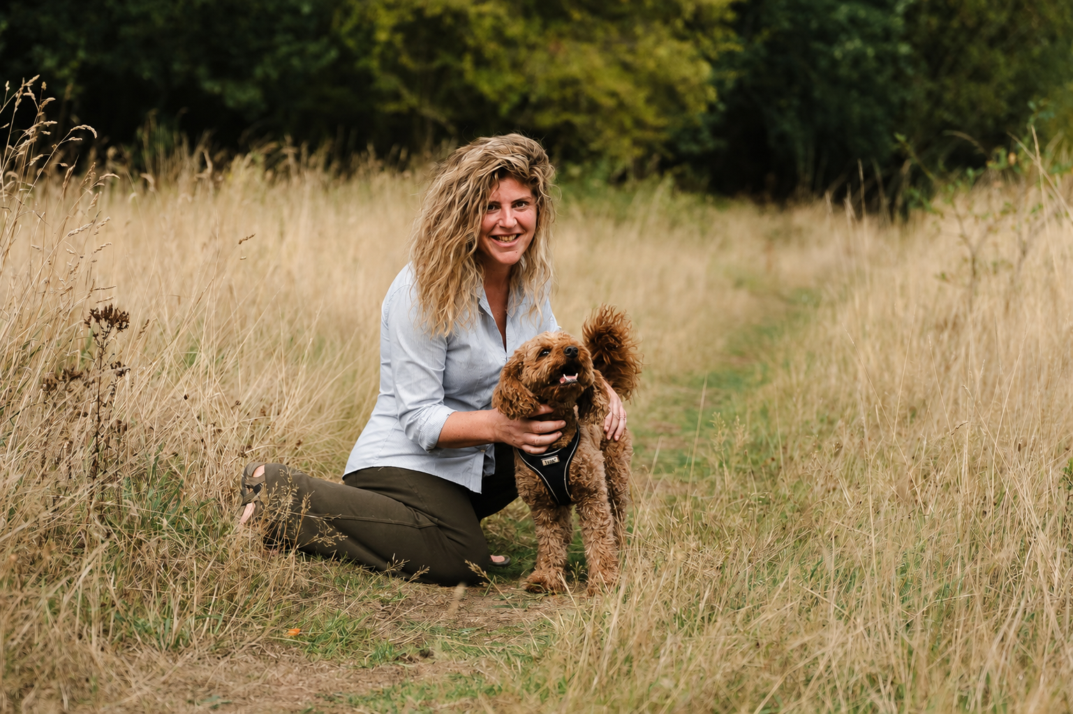 Laura smiling with a dog in a meadow