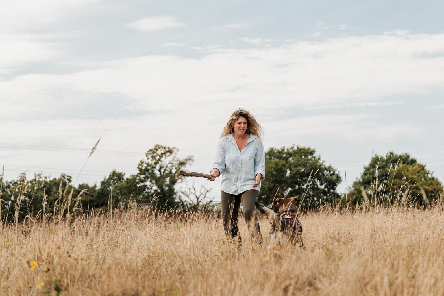 Laura playing in a meadow as a dog runs towards her